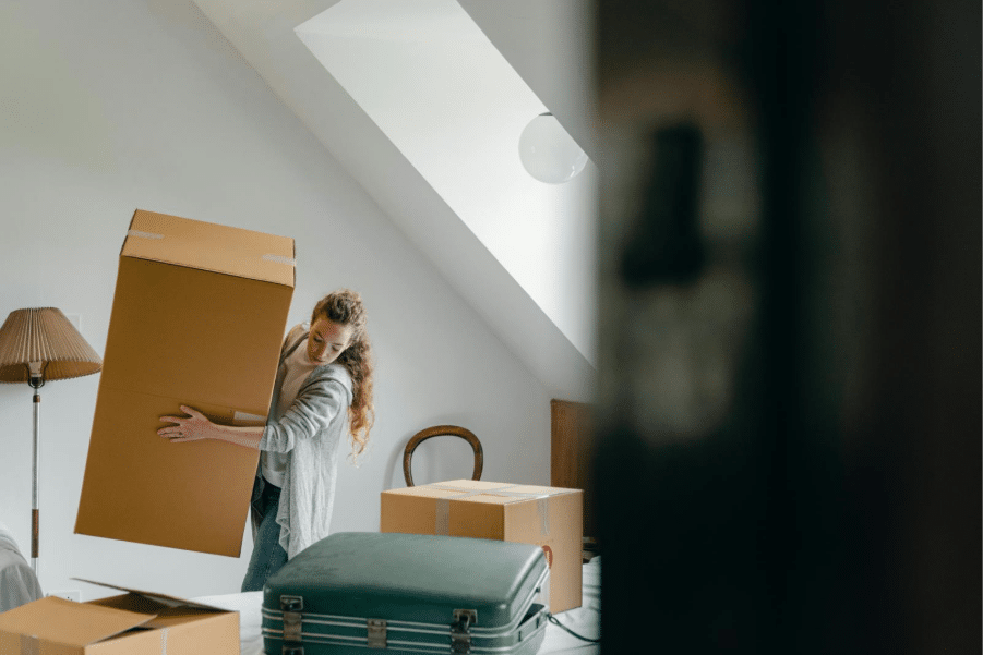 Person lifting cardboard box in a room with packed items, preparing for moving.