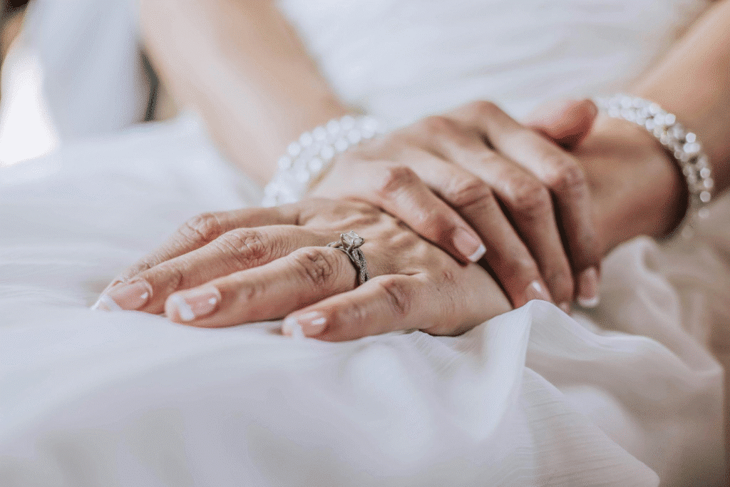 image Close-up of a bride's hands with elegant manicure and diamond engagement ring, resting on a white wedding dress. | Sky Rye Design Close-up of a bride's hands with elegant manicure and diamond engagement ring, resting on a white wedding dress.