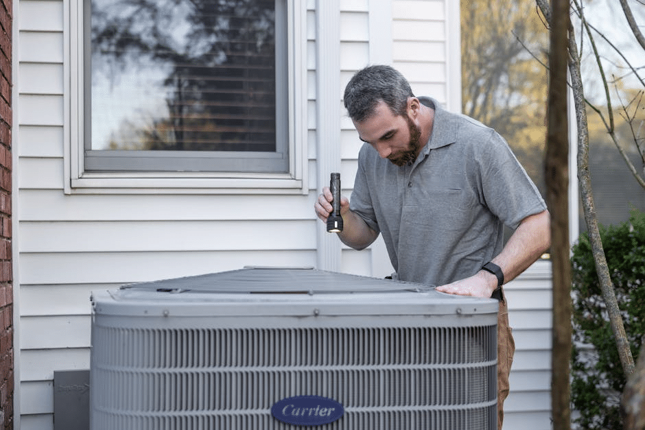 image Technician inspecting outdoor air conditioning unit for maintenance with flashlight. | Sky Rye Design Technician inspecting outdoor air conditioning unit for maintenance with flashlight.