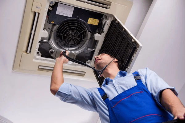 image Technician inspecting ceiling air conditioning unit for maintenance and repair. | Sky Rye Design Technician inspecting ceiling air conditioning unit for maintenance and repair.