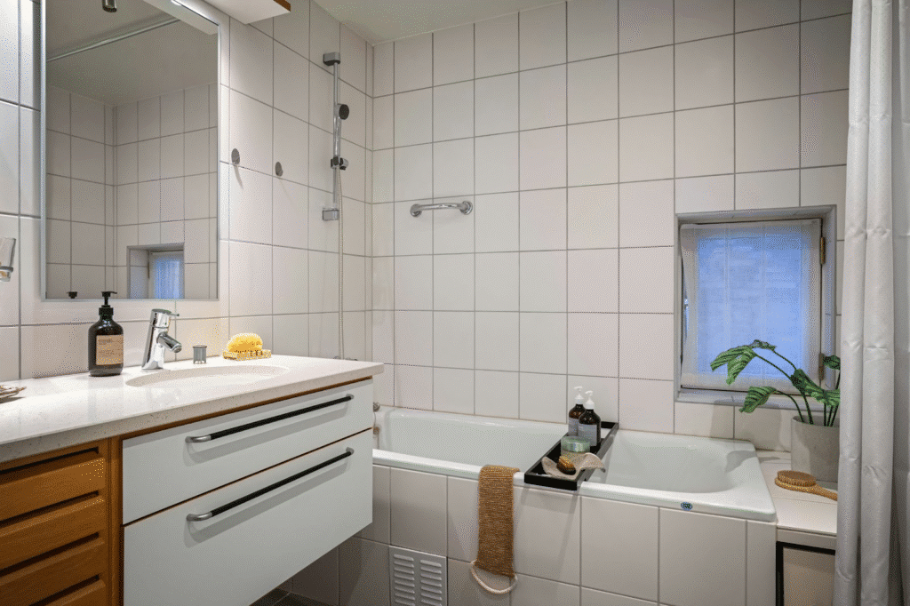 Modern bathroom with white tiles, bathtub, vanity mirror, and plant on window ledge for a fresh look.