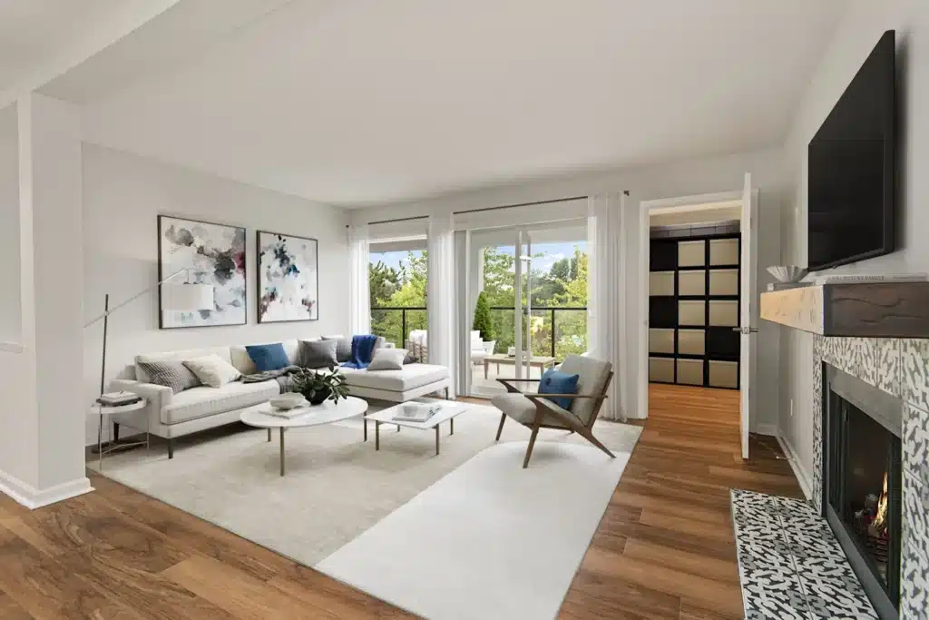 lakeview vs partial living room1 Modern living room with neutral decor, wooden floor, cozy seating, abstract art, and large windows overlooking greenery. | Sky Rye Design Modern living room with neutral decor, wooden floor, cozy seating, abstract art, and large windows overlooking greenery.