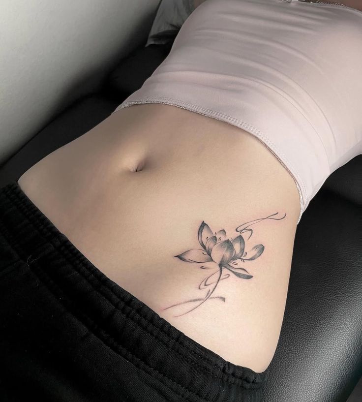 A delicate lotus tattoo on a person's lower abdomen, showcasing intricate black and gray line work.