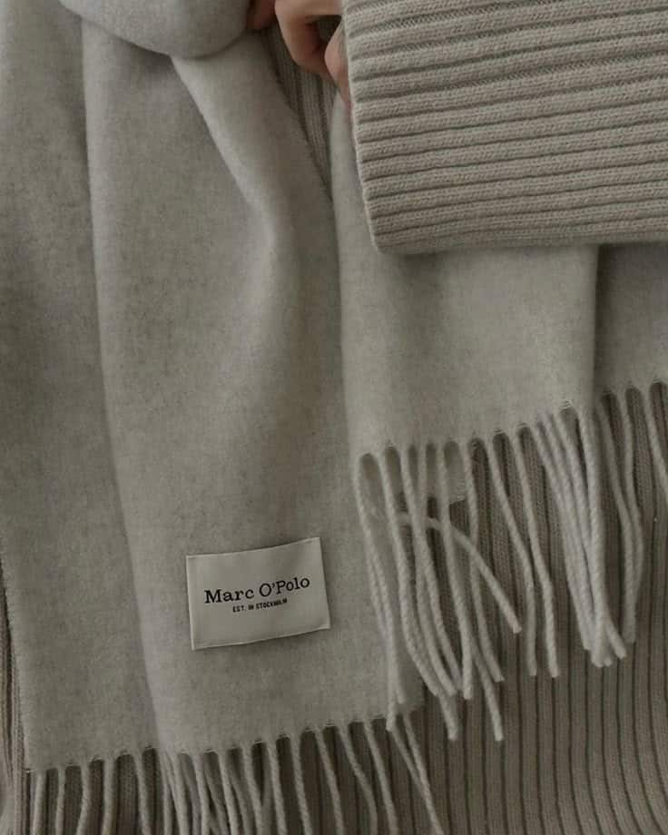 Gray Marc O'Polo scarf with fringes, showcasing soft fabric close-up. Ideal winter accessory for warmth and style.