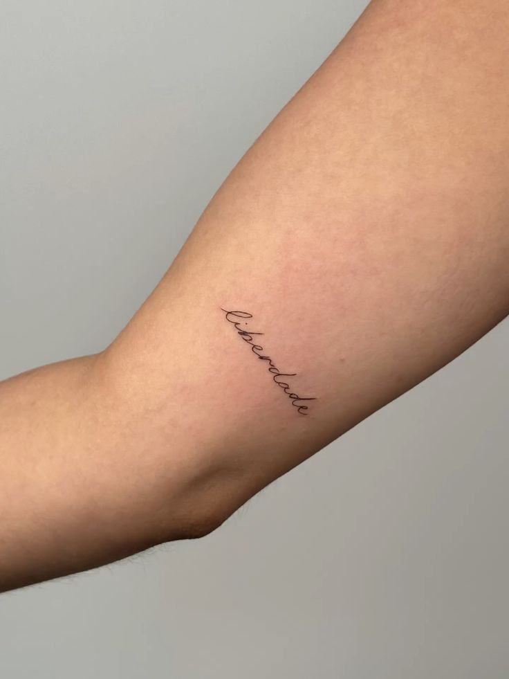 Minimalist liberdade tattoo on inner arm, symbolizing freedom and simplicity in elegant cursive script.