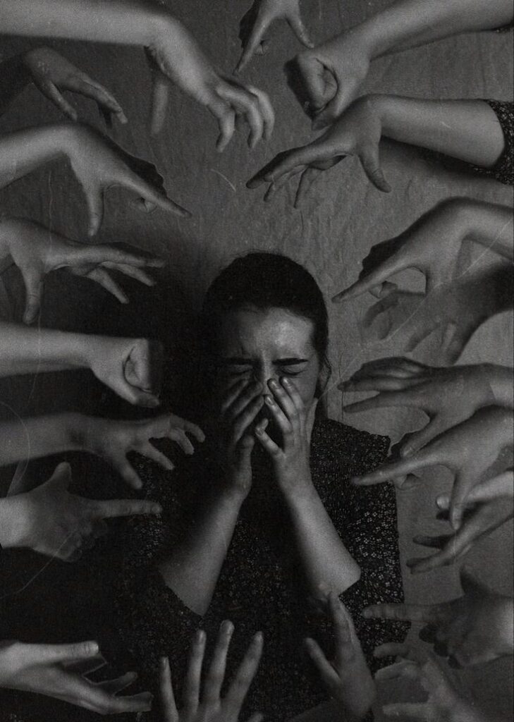 Person overwhelmed by pointing fingers, covering face in distress, symbolizing anxiety and social pressure.