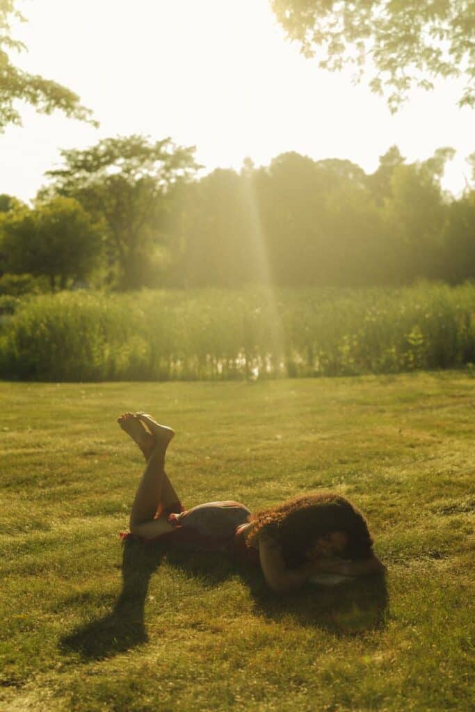 Woman relaxing on sunny grass in a park, with lush greenery and soft sunlight creating a peaceful ambiance.