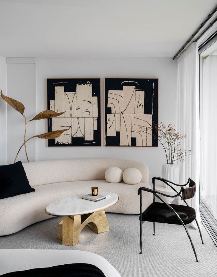 Modern living room with abstract art, curved sofa, gold-accented table, and minimalist decor.