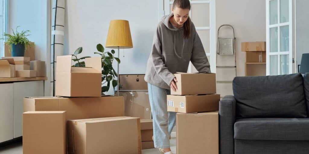 simple-steps-organised-house-move--scaled-2560x1280 Woman moving boxes in a living room filled with cardboard boxes and plants. | Sky Rye Design Woman moving boxes in a living room filled with cardboard boxes and plants.