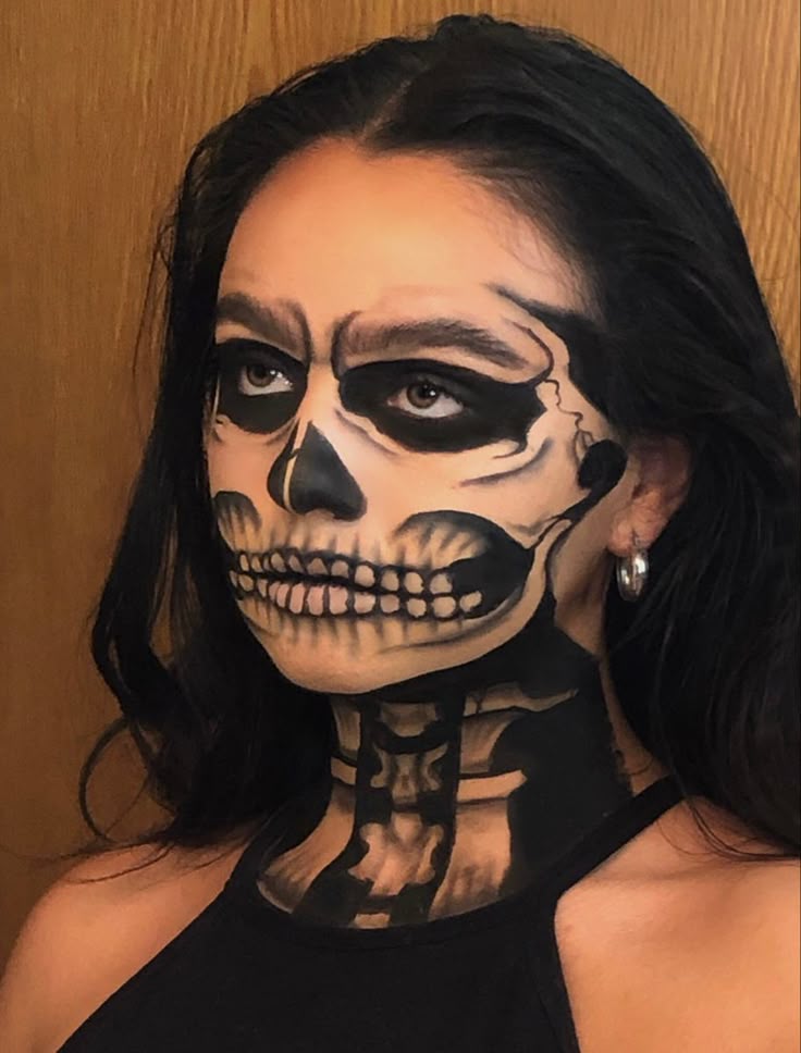 Woman with detailed skull face paint and black dress, looking sideways, perfect for Halloween makeup inspiration.
