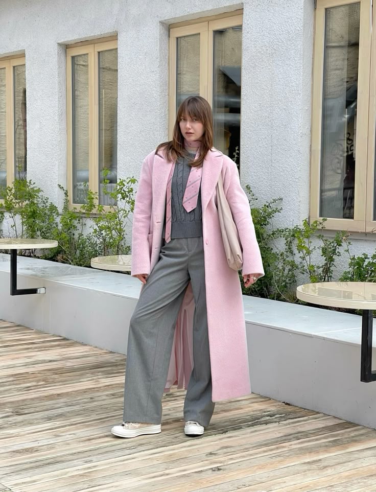 Woman in pink coat and grey outfit standing on wooden deck outside.