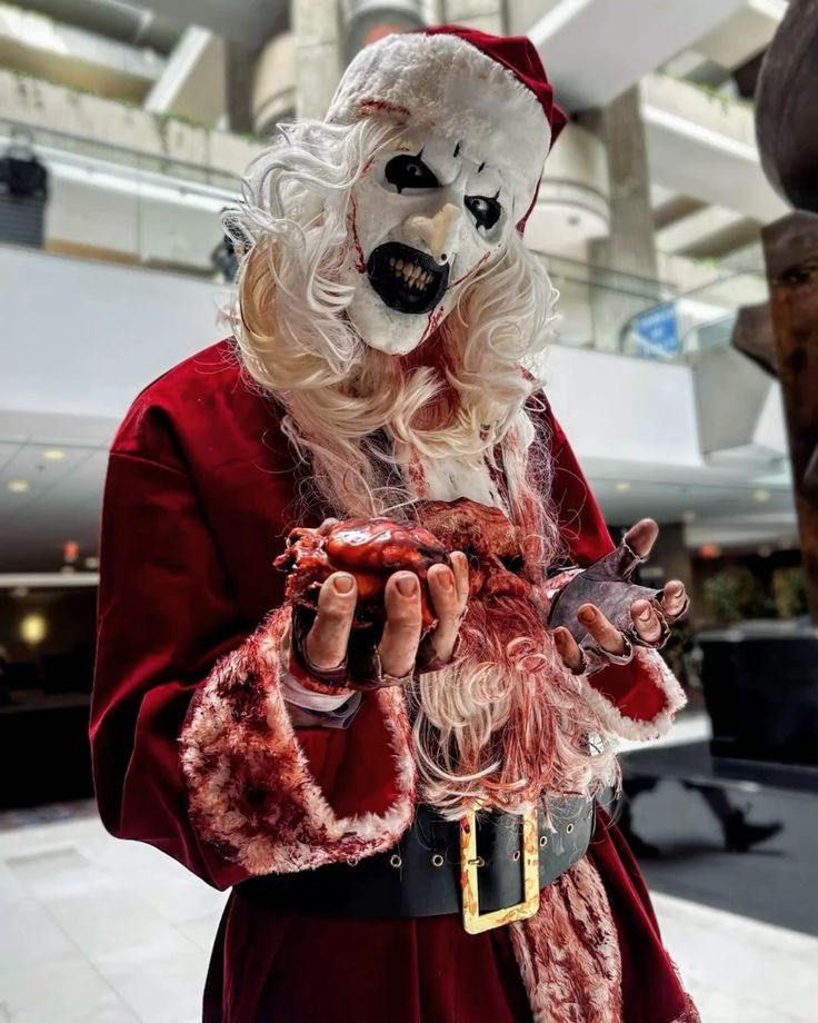 Creepy Santa in a bloody costume holding a fake heart, spooky Halloween cosplay in a festive setting.