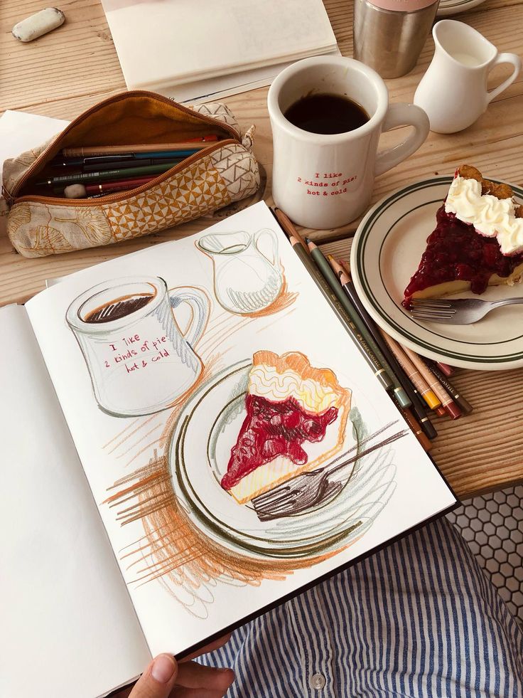 Drawing of pie and coffee with real slice and cup on desk; art supplies nearby. Cozy creative setup.