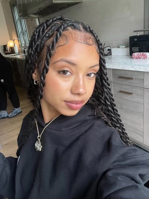 Young woman with braids and black hoodie in a modern kitchen, looking towards the camera.