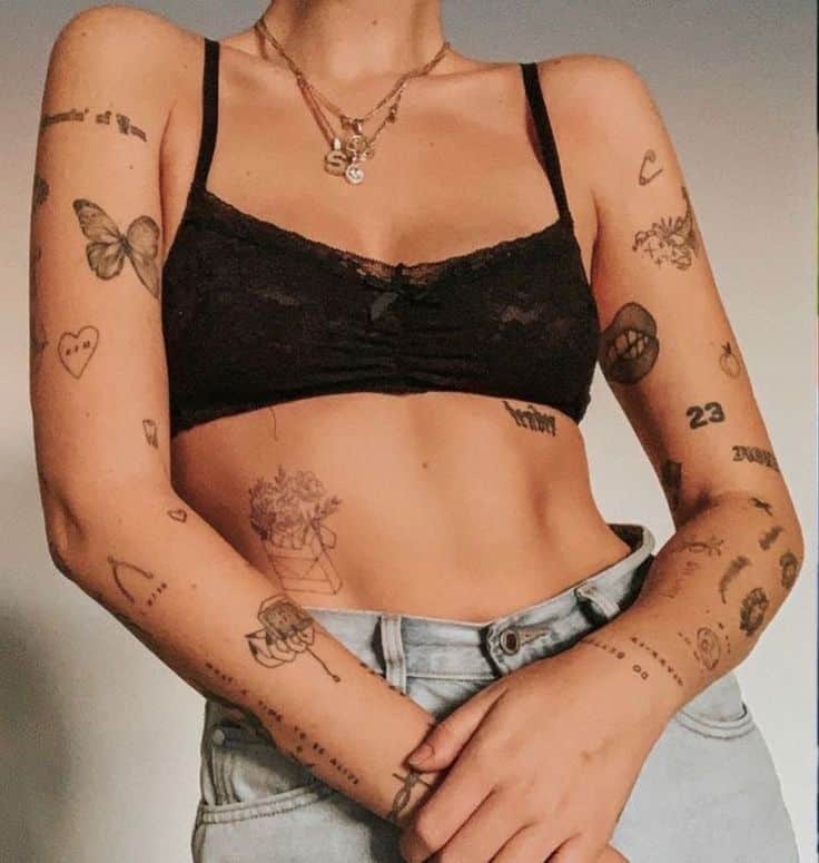 Person wearing a black crop top and jeans, showcasing various artistic tattoos on arms and midriff.
