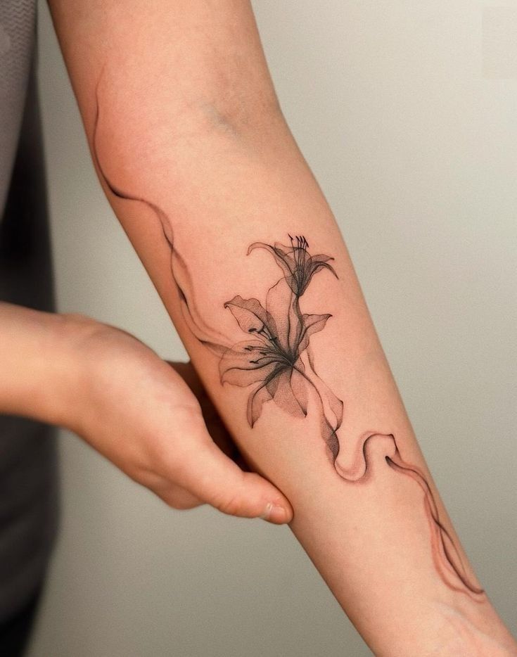 Delicate floral tattoo on forearm with flowing lines and intricate design, held gently by hand.