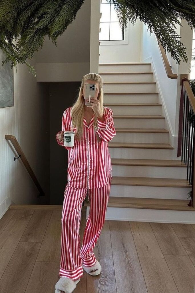 Woman in red and white striped pajamas taking a mirror selfie on stairs, holding a coffee mug.