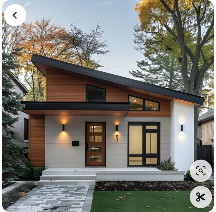 Modern home with sloped roof, large windows, and vibrant autumn trees in the background.