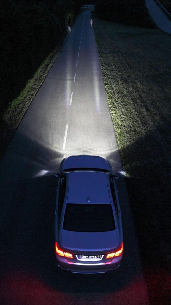 _ Car driving on dimly lit road at night, headlights illuminating pedestrians ahead. | Sky Rye Design Car driving on dimly lit road at night, headlights illuminating pedestrians ahead.
