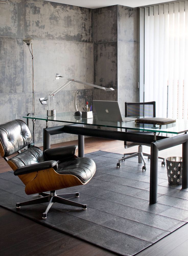 Modern office with glass desk, ergonomic chairs, and industrial decor, featuring a laptop and desk lamp.