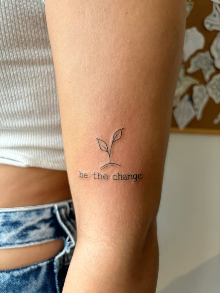Arm tattoo with a small sprout and the phrase be the change, symbolizing growth and positive transformation.
