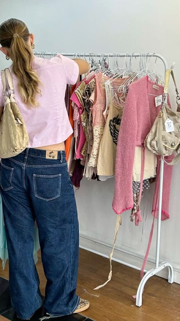 Woman browsing colorful clothes on a rack in a store, wearing jeans and a pink top.
