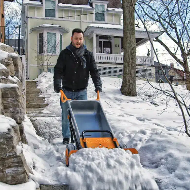 Man clearing snow with a wheeled snow remover outside a house.