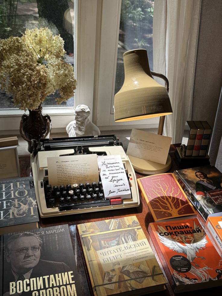 Vintage typewriter on a desk with books and a lamp, creating a nostalgic writing nook by a window.