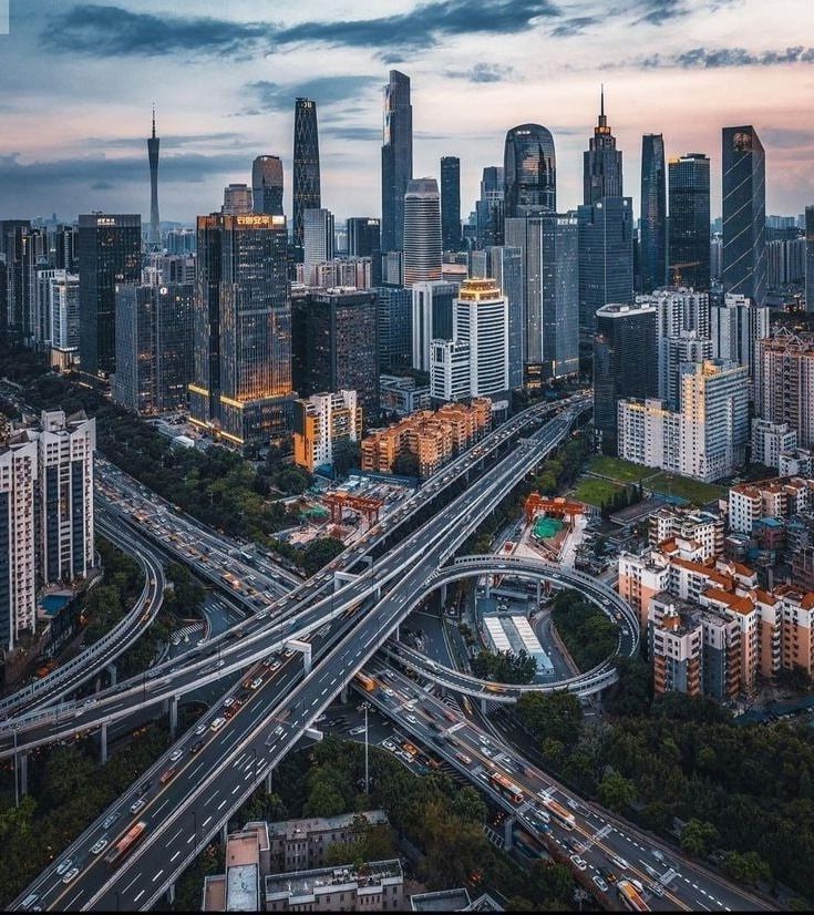 Aerial view of a modern cityscape with towering skyscrapers and intricate highway intersections at dusk.