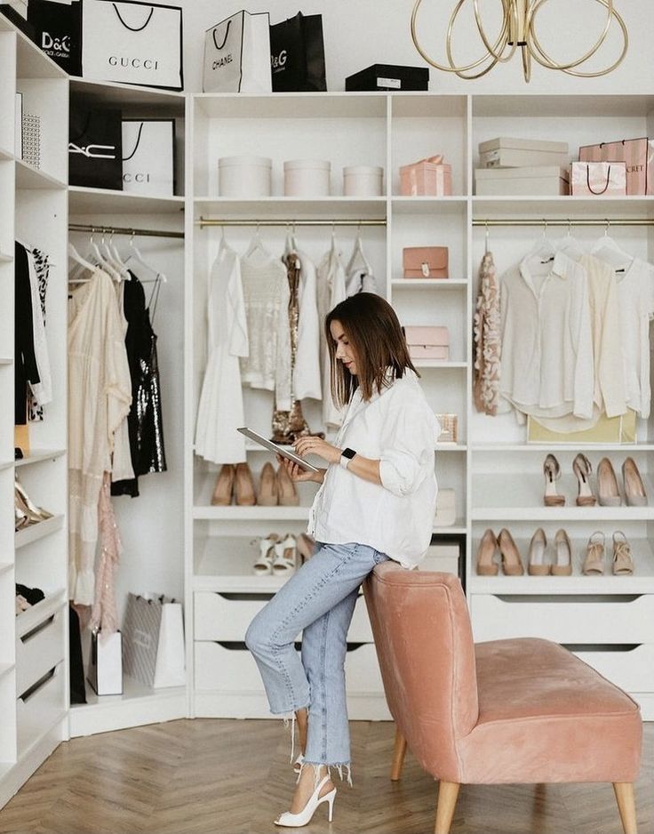 Woman browsing on tablet in elegant walk-in closet with fashion items and designer shopping bags.