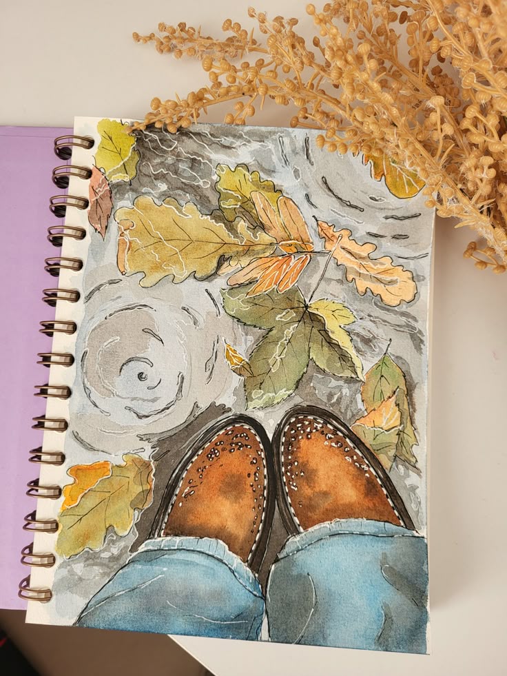 Watercolor painting of brown shoes and autumn leaves on a sketchbook with dried flowers nearby.