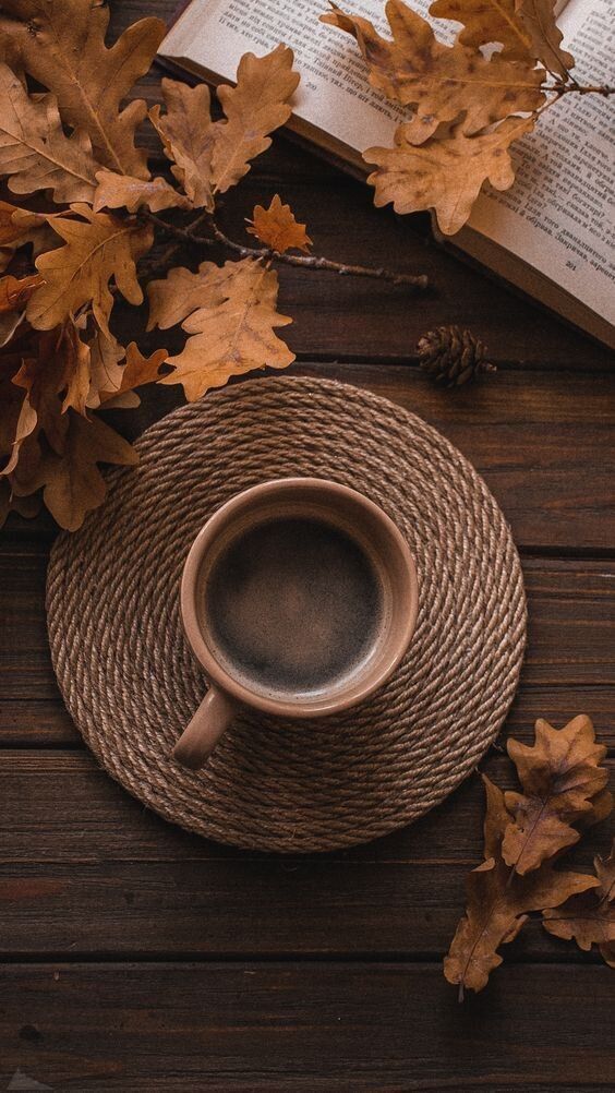 Cozy autumn setup with coffee cup, open book, and oak leaves on a wooden table.