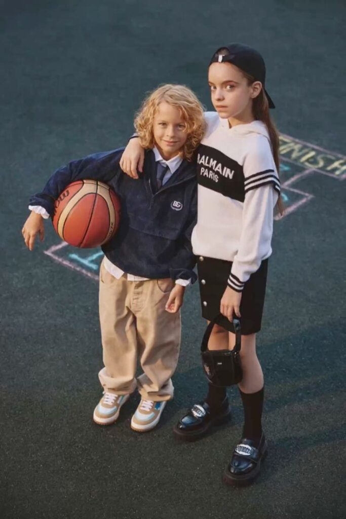 Two stylish kids pose on a basketball court, one holding a basketball. Casual and trendy fashion.