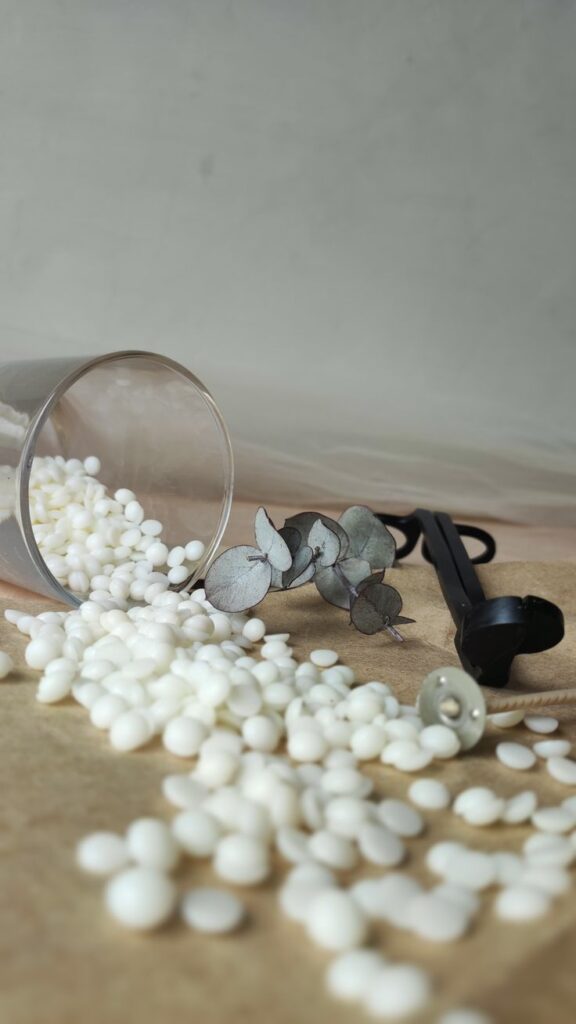 Spilled white wax pellets with eucalyptus leaves and a candle wick on a table.