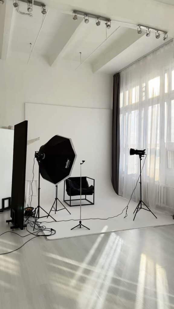 Photography studio with lighting equipment, black chair, and large windows.
