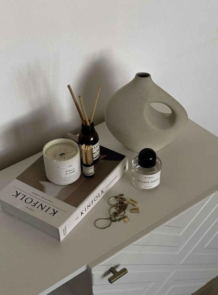 Modern minimalist decor: vase, candle, perfume, book, and jewelry on a white cabinet. Clean, elegant design.