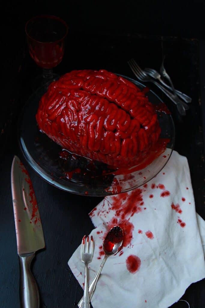 завантаження Realistic brain-shaped gelatin dessert with red glaze, surrounded by a knife and utensils on a dark table setting. | Sky Rye Design Realistic brain-shaped gelatin dessert with red glaze, surrounded by a knife and utensils on a dark table setting.