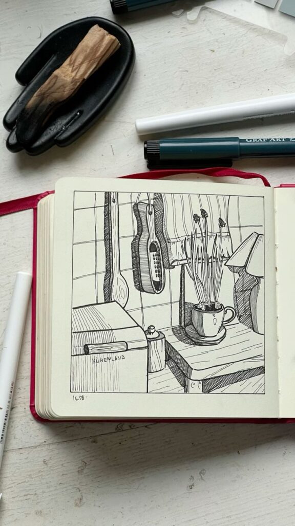 скетч скетчинн Black ink sketch of a coffee mug and utensils on a table, with a guitar hanging nearby, in an open notebook. | Sky Rye Design Black ink sketch of a coffee mug and utensils on a table, with a guitar hanging nearby, in an open notebook.