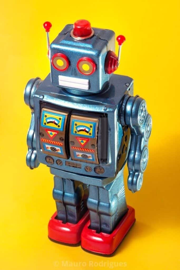 Vintage tin robot toy with red feet and colorful dials against a vibrant yellow background.