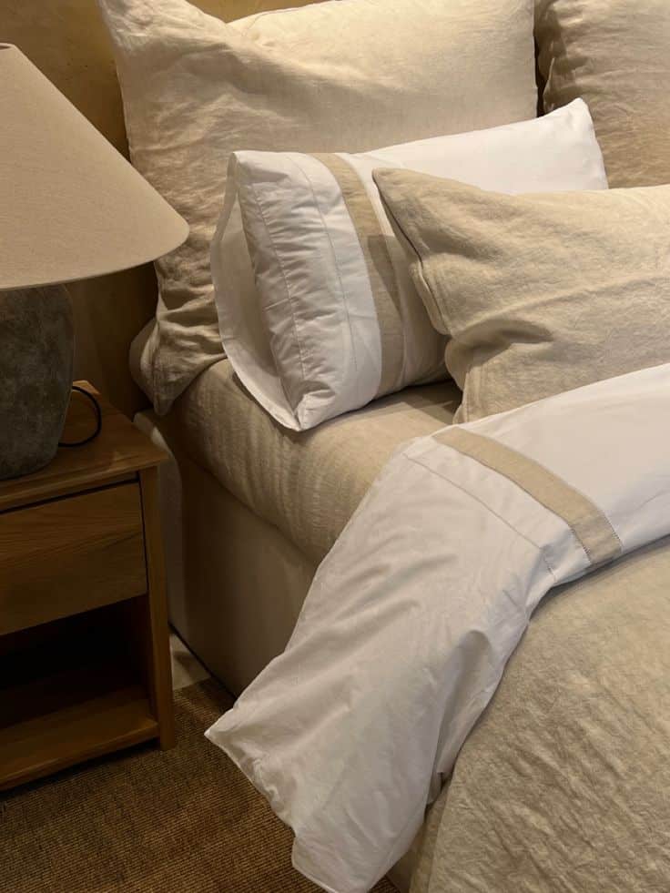 Cozy beige bedding with fluffy pillows and a bedside lamp, creating a warm and inviting bedroom atmosphere.
