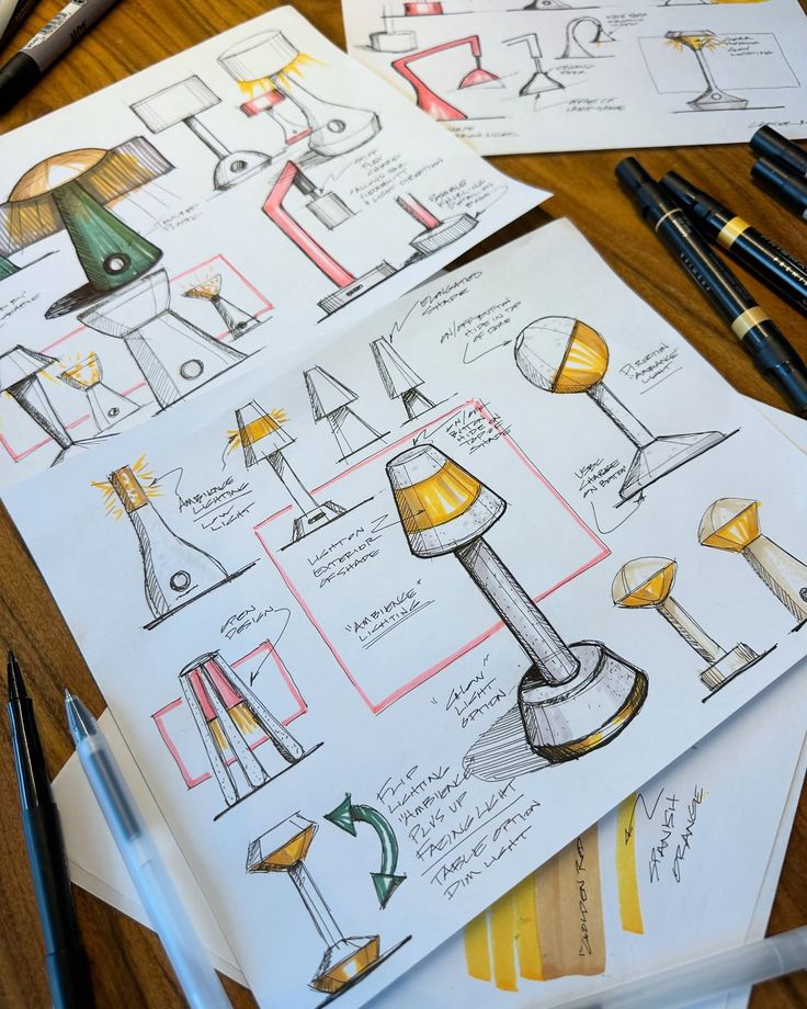 ✈️ Travel Sketching ✍🏼 Project _ Table Top Hand-drawn sketches of futuristic table lamp designs on a wooden desk with markers. | Sky Rye Design Hand-drawn sketches of futuristic table lamp designs on a wooden desk with markers.
