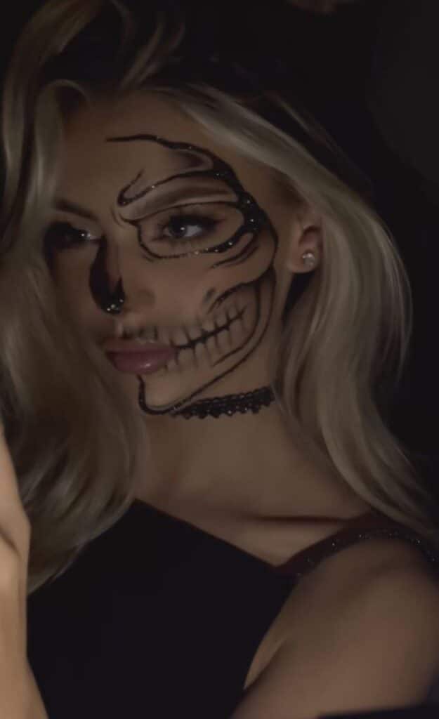 Woman with skeleton makeup and choker necklace, posing in dark lighting. Spooky Halloween face paint.