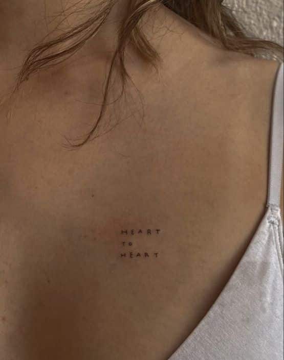 Heart to Heart tattoo on collarbone, wearing a white tank top. Minimalistic script, intimate message, personal expression.