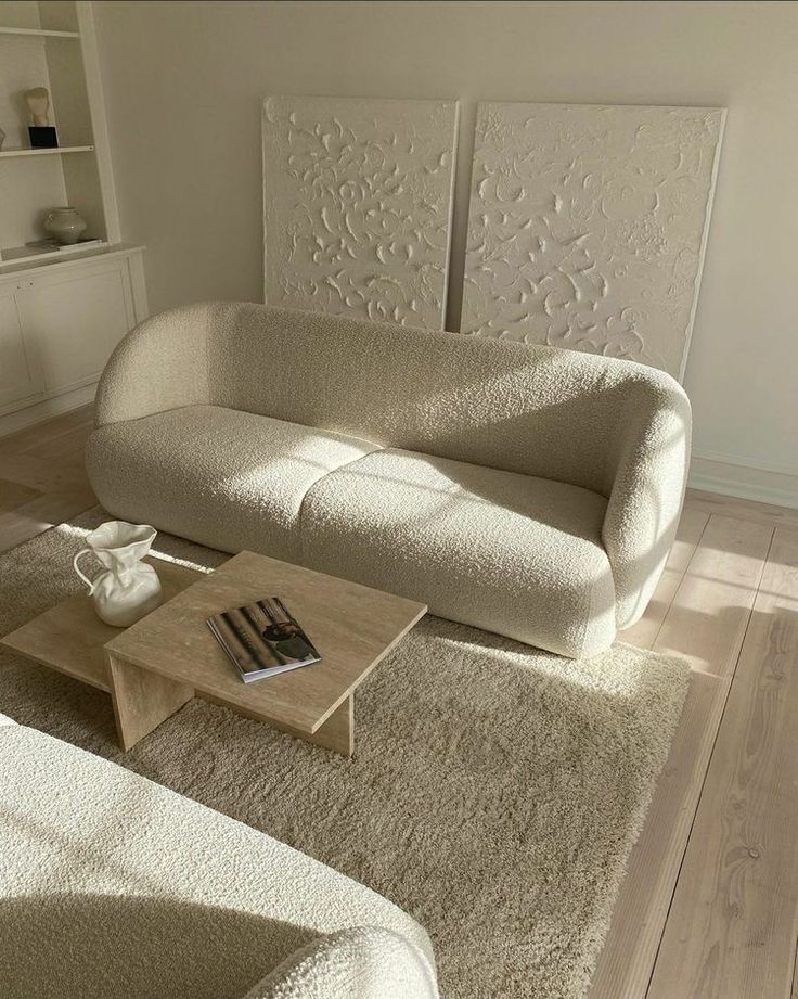 Modern living room with beige curved sofa, textured wall art, and minimalist coffee table on a cozy rug.