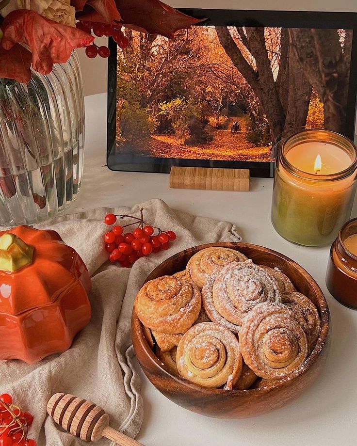 Cozy autumn decor with cinnamon rolls, lit candles, and a scenic tablet image creating a warm ambiance.