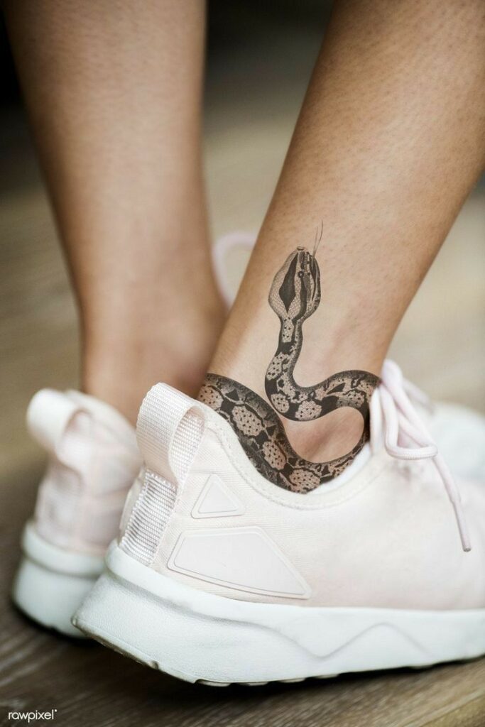 тату татуировка tattoo змея snake татуировка на ноге tattoo on leg эстетика aesthetics Ankle tattoo of a snake with pink sneakers on wooden floor, showcasing unique body art and fashion. | Sky Rye Design Ankle tattoo of a snake with pink sneakers on wooden floor, showcasing unique body art and fashion.