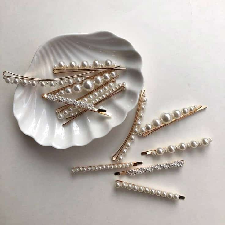 𝒾𝓃𝓈𝓈 Gold and pearl hair clips in a white seashell dish, elegantly arranged on a table. | Sky Rye Design Gold and pearl hair clips in a white seashell dish, elegantly arranged on a table.