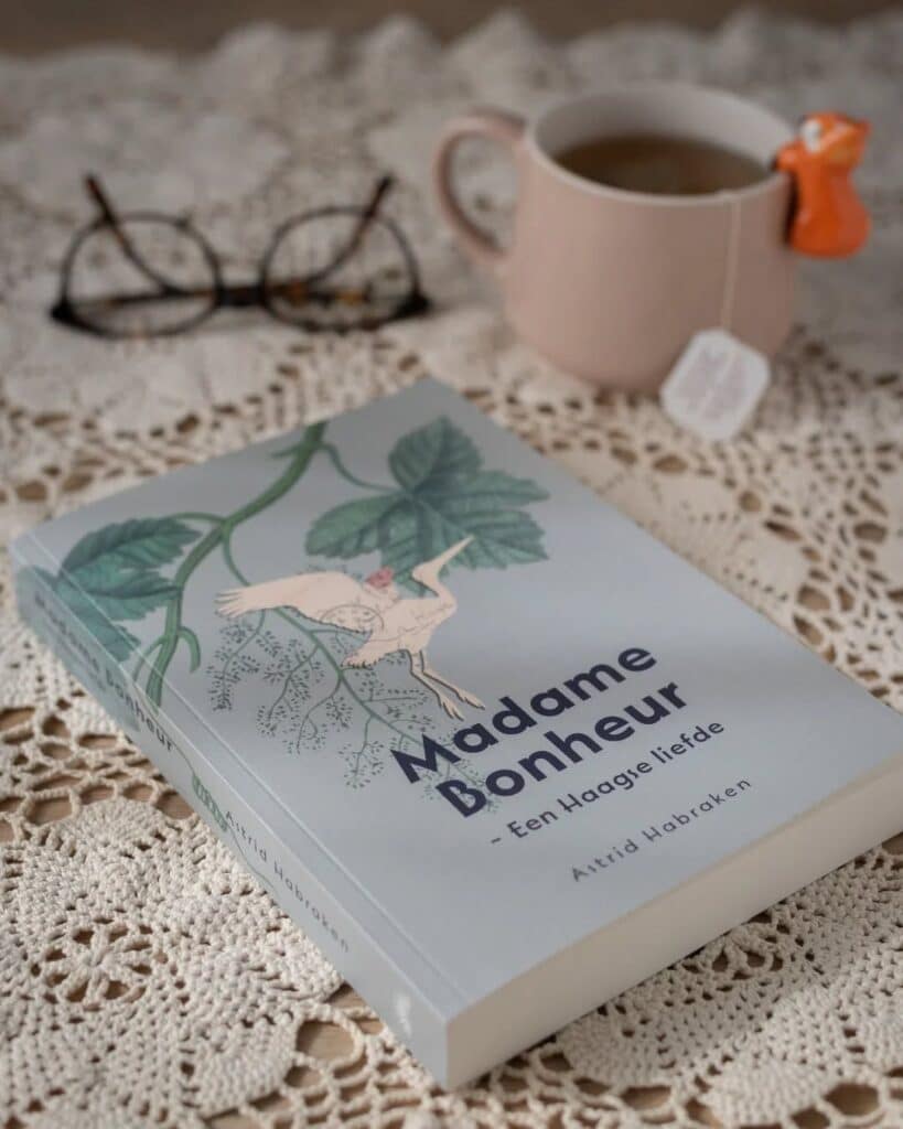 Book Madame Bonheur on crochet cloth with glasses and tea, invoking cozy reading ambiance.