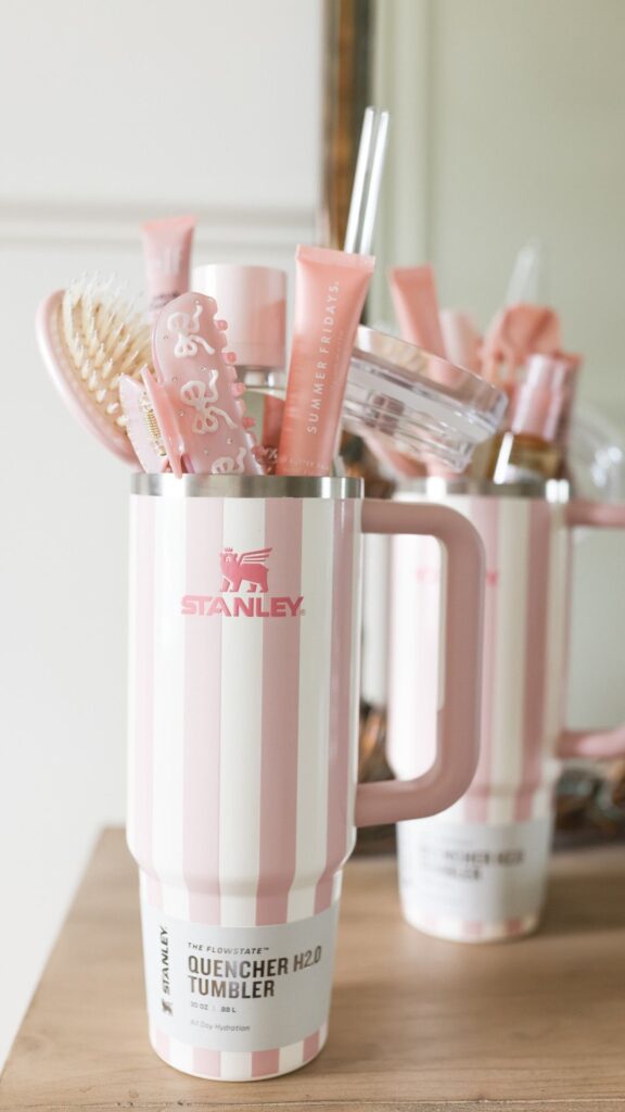 Pink striped Stanley tumbler filled with beauty products on a wooden surface, reflecting a chic and organized setup.