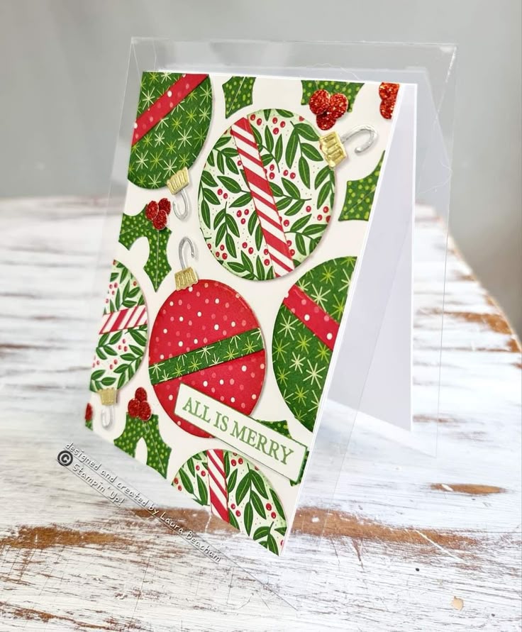 Festive Christmas card with colorful ornament designs and All is Merry text on a rustic wooden table.